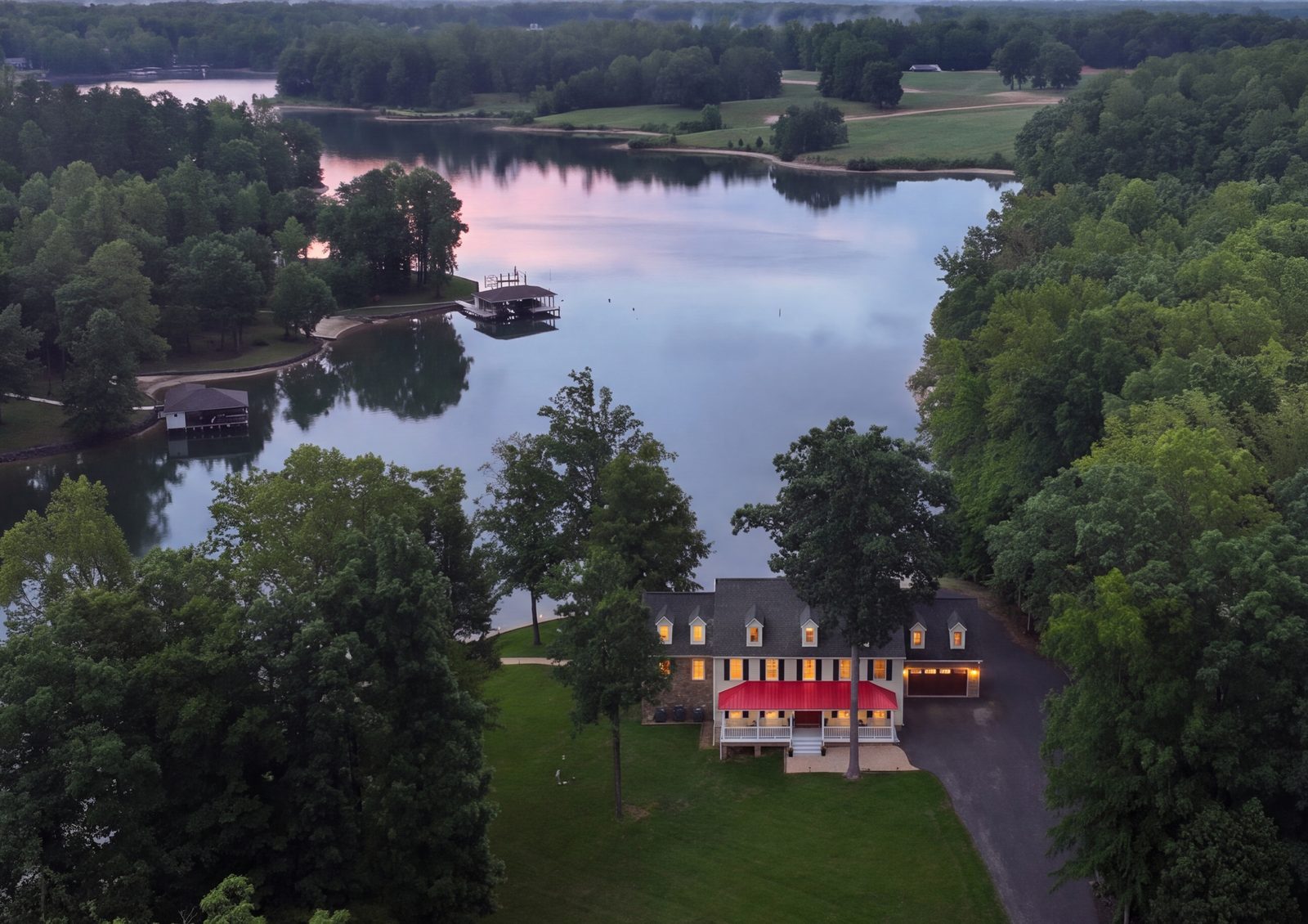 Twilight aerial of the lit yellow beach house above quiet lake coves